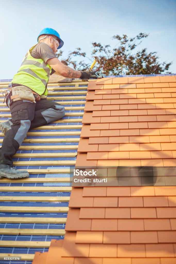 a roofer nails on the roof tiles